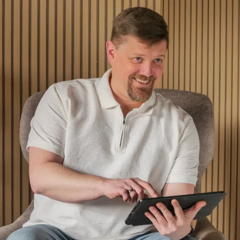 Mann in einem Sessel, der auf einem Tablet tippt und dabei lächelt.