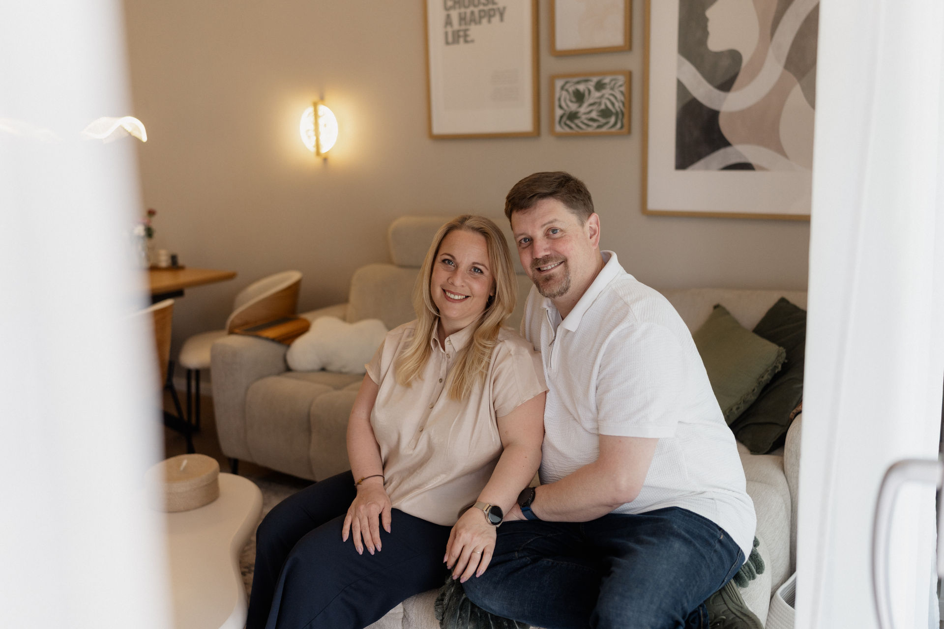 Sarah und Manuel von &oh, lächelnd nebeneinander auf einem hellen Sofa